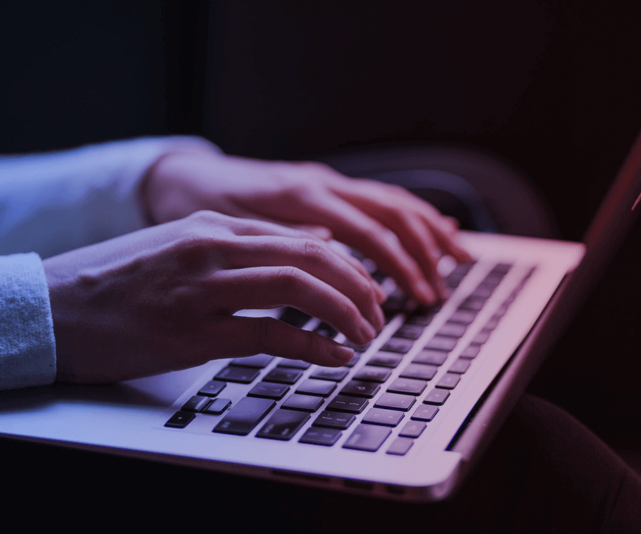 Photograph of woman's hands writing on a laptop's keyboard with a purple filter