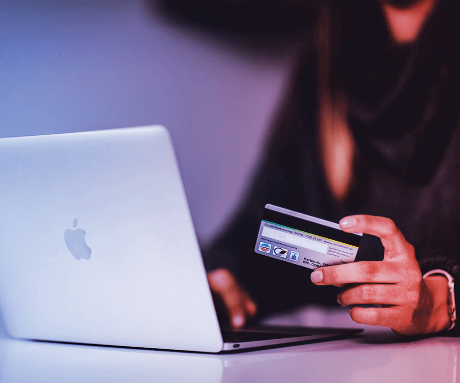 Photograph of a woman with a credit card on her hand writing on a laptop's keyboard