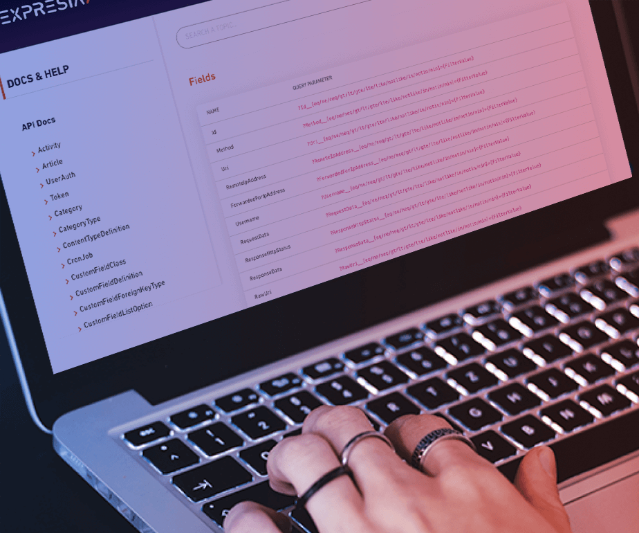 Open laptop photograph under a hand with rings writing on the keyboard with a purple and pink filter